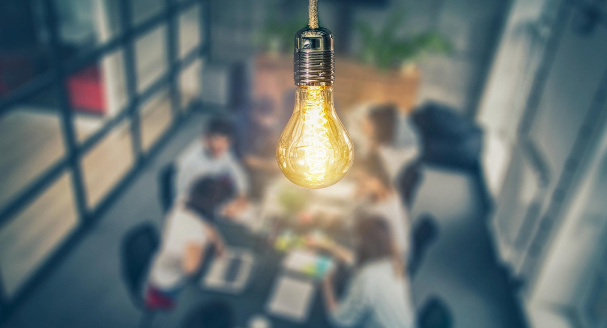 Close up of light bulb with group meeting below