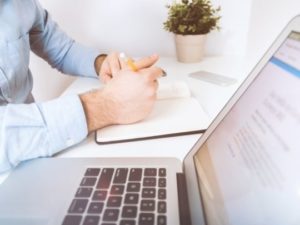 Man writing in a notebook next to a laptop