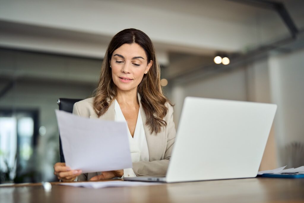 Business woman looking at paper sitting by laptop