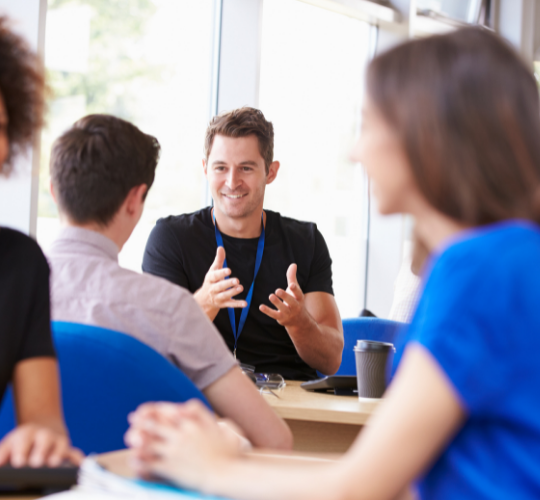 Man wearing black tshirt, blue lanyard, smiling with hands up